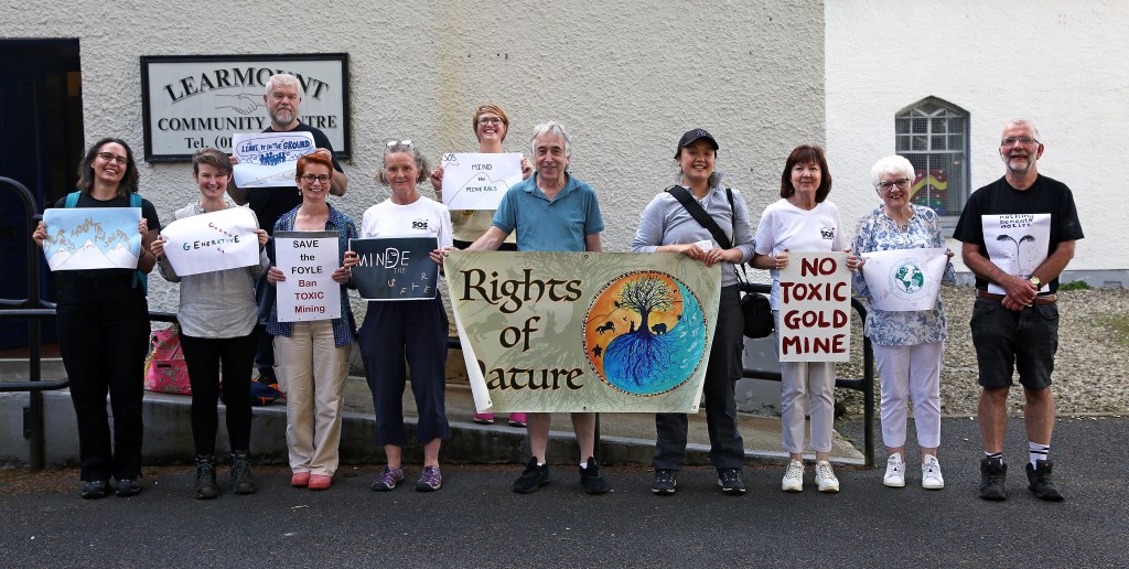 Photo of workshop participants and SOS community activists outside the Learmont Community Centre holding up posters of the postcard designs made during Conor Nolan's workshop